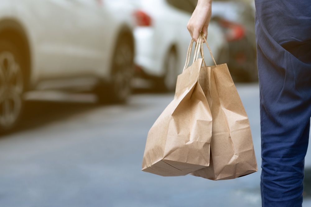 A walking person holds two bags of takeout food