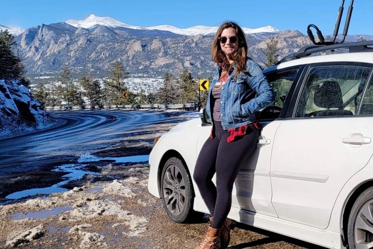 Digital nomad Jess Goudreault stands by her car in Denver, Colorado, with beautiful mountain views in the background.